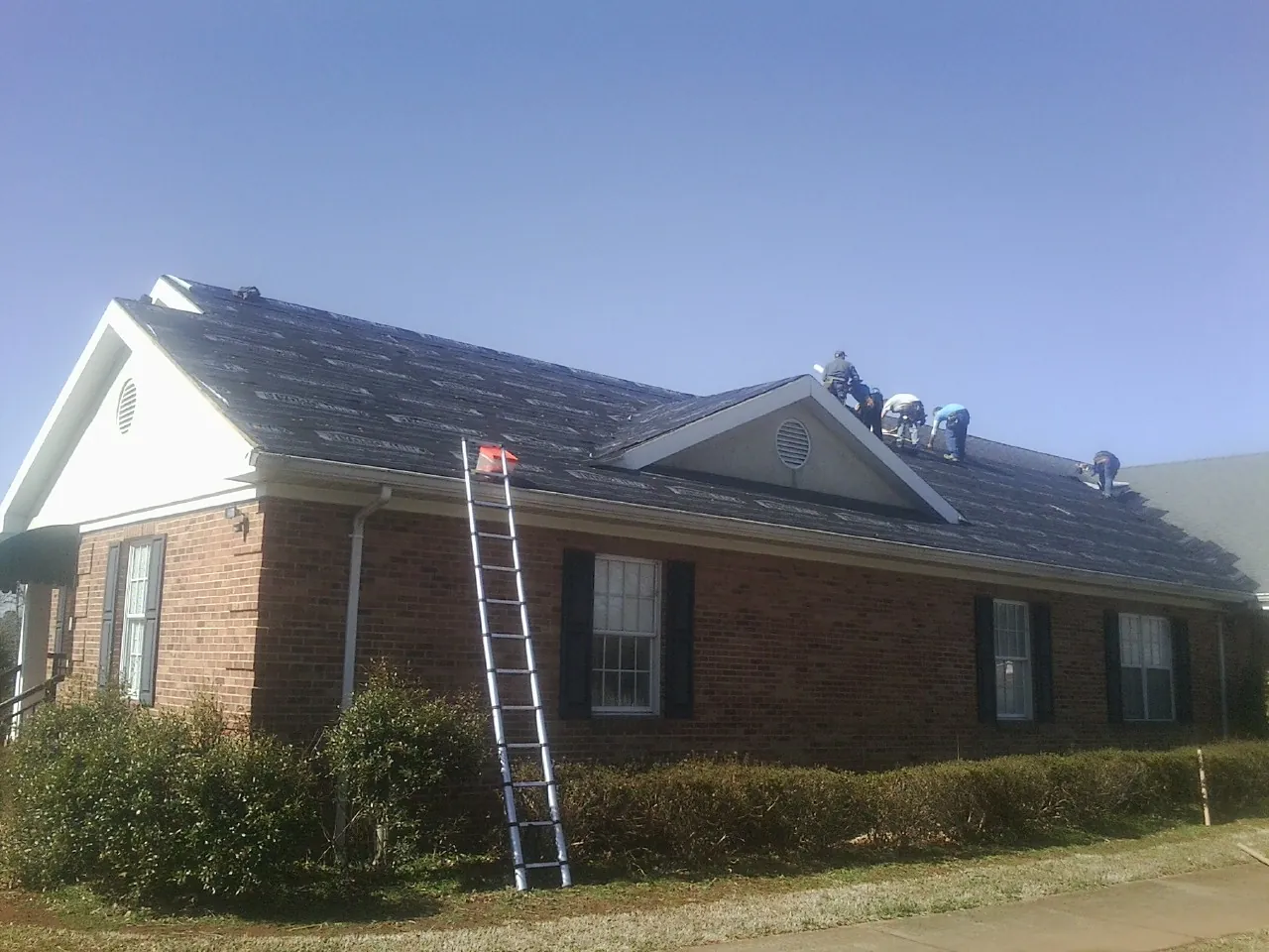 Crew tearing shingles off a brick ranch roof with a ladder set — Emergency Roof Repair work by our crew in Rex