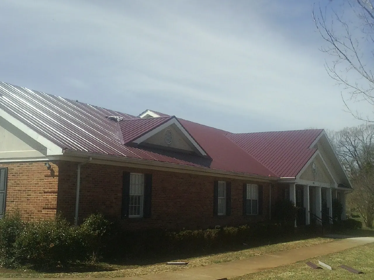 Red metal roof with gabled entries on a long brick building, from a Hail Damage Roof Repair job in Rex