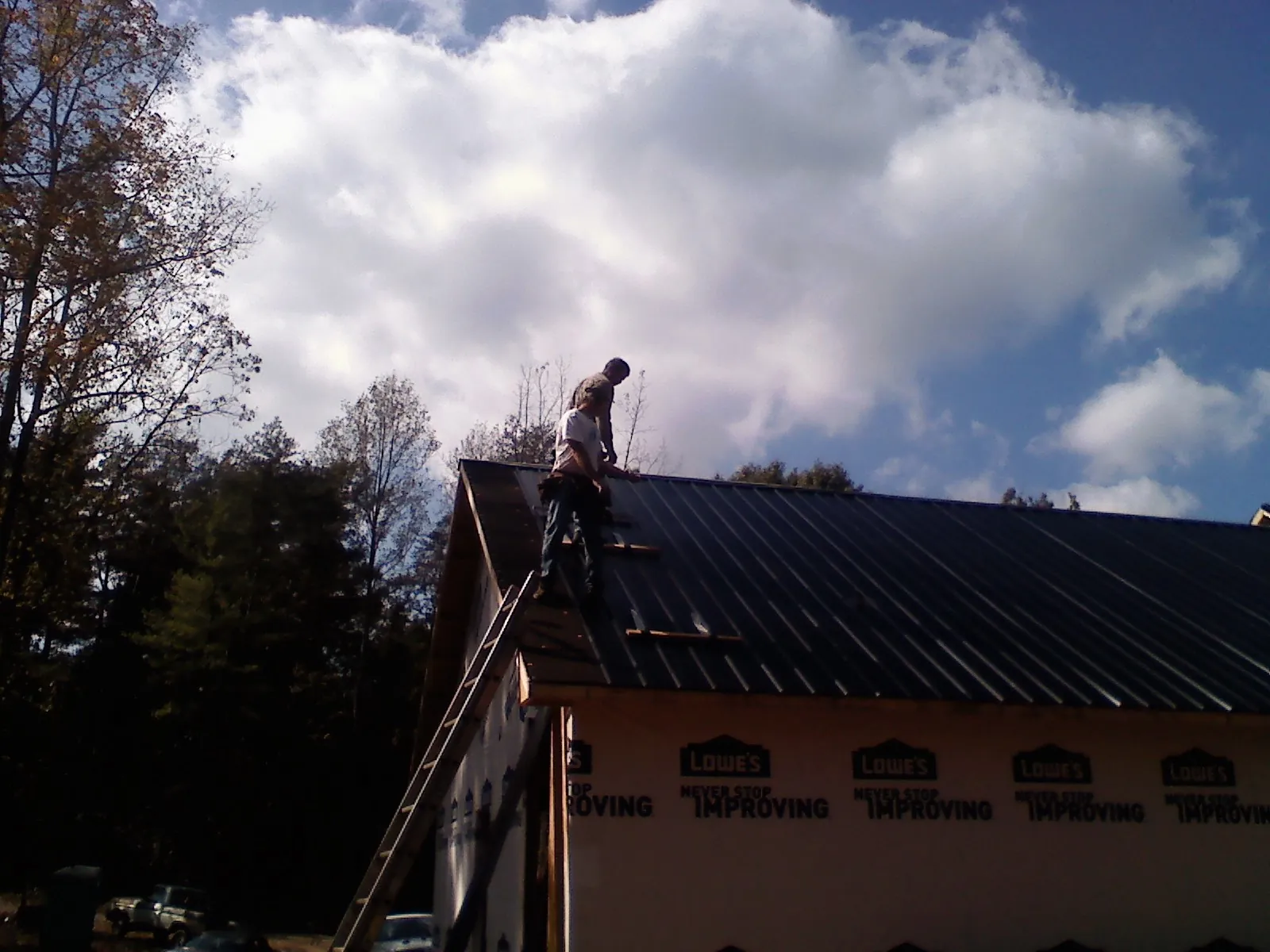 Roofer fastening dark metal panels high against a cloudy sky, from a Roof Inspection job in Rex